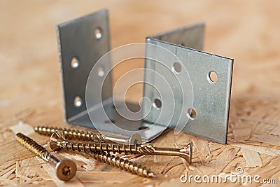 Two galvanized angle brackets and self drilling screws lying on chip board. Blurred background Stock Photo