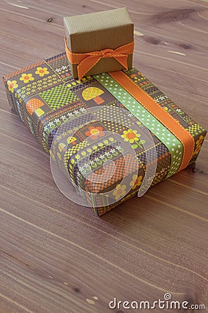 Two gifts in vintage wrapping paper with flowers and mushrooms, green brown and orange, neutral wood background Stock Photo