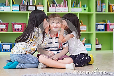 Two girl kids whisper secret at ear of boy in library at kindergarten preschool,Fun and happy children,back to school concept Stock Photo