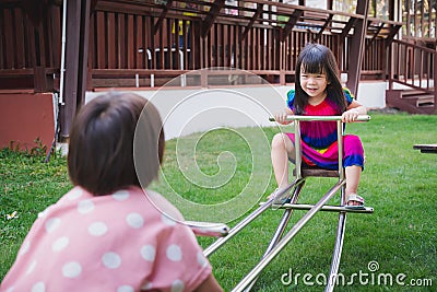 Two girl siblings playing teeter totter rocking with joy. Asian child have sweet smile. Children laughed brightly. Stock Photo