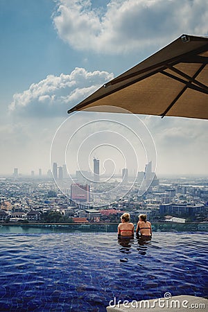 Two Girls in Bikinis Swimming in Infinity Pool Overlooking Bangkok Thailand Urban City Landscape Luxurious Vacation Destination Editorial Stock Photo