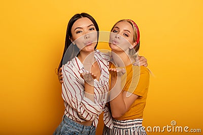 Two girls send kiss to social friends. Emotional and joyful expression. Yellow background Stock Photo