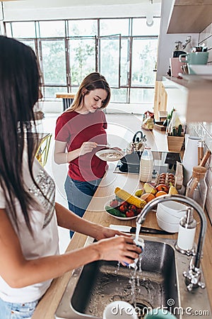 Two girls friends in kitchen preparing breakfast cooking and washing dishes Stock Photo