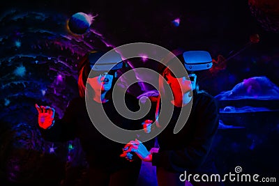 Two girls friends in virtual glasses are holding hands in the playroom in neon light Stock Photo