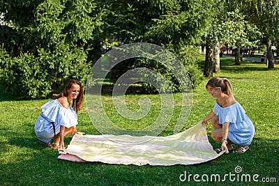 Two girls on a green meadow spread out a picnic blanket. Summer weekends Stock Photo