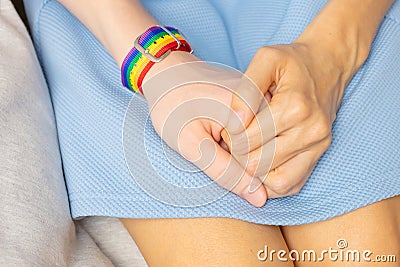 Two girls are holding hands, on one hand there is LGBT bracelet. Stock Photo