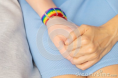 Two girls are holding hands, on one hand there is LGBT bracelet. Stock Photo