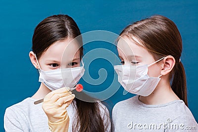 Two girls in medical masks are examining a coronavirus which one of them holds in tweezers. Hand in latex glove. Stock Photo