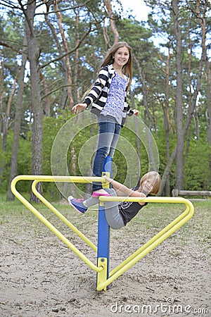 Two girls are playing on the playground on the yellow metal attraction. It's windy. Stock Photo