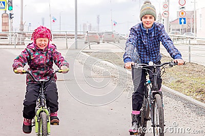 Two happy girls sisters on a spring walk roll down the hill on their bicycles. Stock Photo