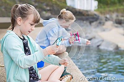 Two Girls Sitting On Harbour Wall Catching Crabs Stock Photo