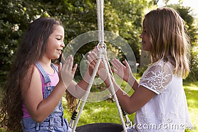 Two Girls Sitting On Swing Playing Clapping Game Stock Photo