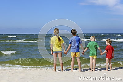 Two girls and two boys in colorful t-shirts standing back on a sandy beach Stock Photo