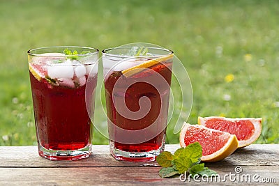 Two glasess with grapefruit drinks, wooden table, green garden background Stock Photo