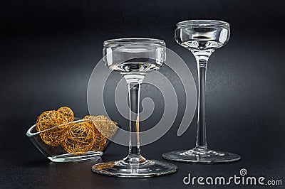 Two glass candlesticks standing on a black, shiny background, next to a small vase with metal golden balls. Stock Photo