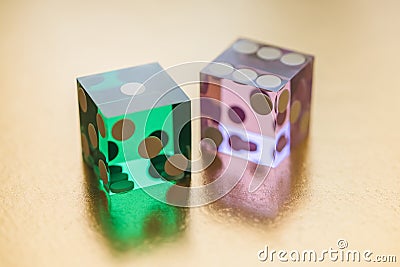 Two glass dice, green and pink, on a gold background in sunlight. Result one and six. Stock Photo