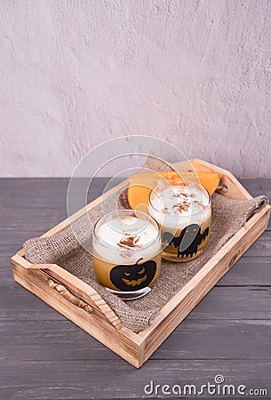 Two glass glasses with Halloween-themed drawings with pumpkin latte on a wooden tray. Drinks for Halloween Stock Photo