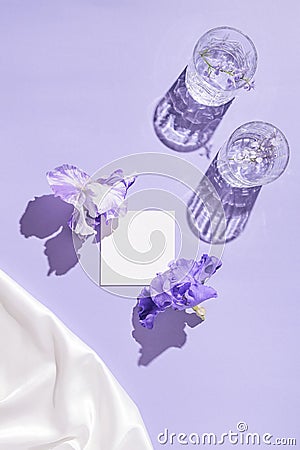 Two glasse with water and card note with flowers on pastel lilac background with white silk cloth. Summer refreshment concept Stock Photo