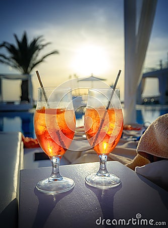 Two glasses with Aperol Spritz aperitif cocktail consisting of prosecco, Aperol and soda water near a swimming pool at sunset Stock Photo