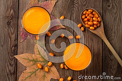 Two glasses of fresh natural sea buckthorn juice, with autumn leaves and sea buckthorn berries and wooden spoon. Stock Photo