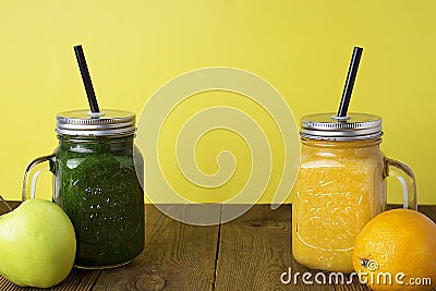 Two glasses with green and yellow detox smoothie with straws. Spinach and pumpkin smoothie on wooden table. Copy space Stock Photo