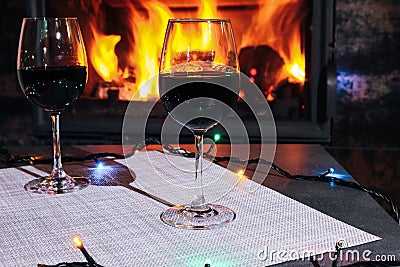 Two glasses of red wine against the background of a burning fireplace in hard reflective lighting. Romantic relaxed dinner by the Stock Photo