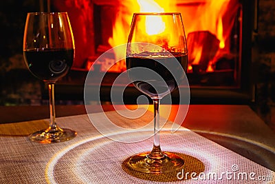 Two glasses of red wine against the background of a burning fireplace in hard reflective lighting. Romantic relaxed dinner by the Stock Photo