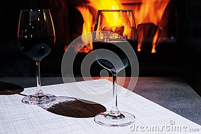 Two glasses of red wine against the background of a burning fireplace in hard reflective lighting. Romantic relaxed dinner by the Stock Photo