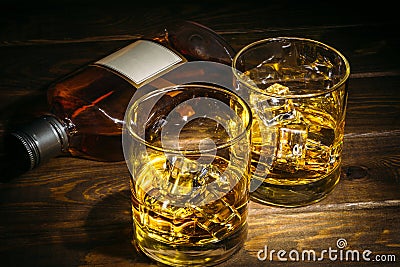 Two glasses of scotch whiskey or cognac with ice cubes and bottle of alcohol liquor on dark wooden background Stock Photo