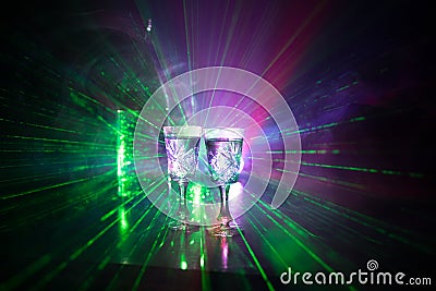 Two glasses of Vodka with bottle on dark foggy club style background with glowing lights (Laser, Stobe) Multi colored. Club drinks Stock Photo