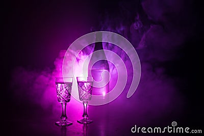 Two glasses of Vodka with bottle on dark foggy club style background with glowing lights (Laser, Stobe) Multi colored. Club drinks Stock Photo