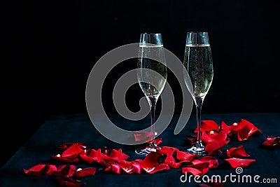 Two glasses with white champagne and petals of red roses on the black background Stock Photo