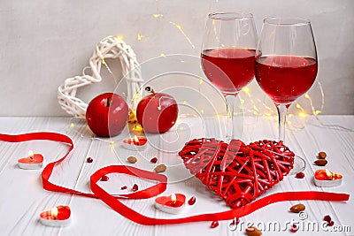 Two glasses of wine, red hearts, ribbons, apples on a light background with garlands for Valentine`s Day Stock Photo