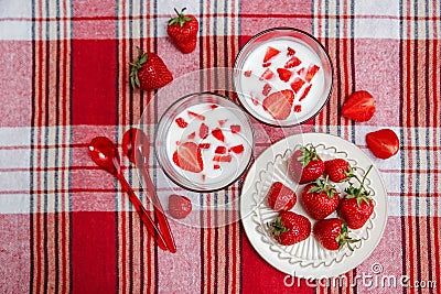 Two Glasses of Yogurt,Red Fresh Strawberries are in the Ceramic Plate with Plastic Spoons on the Check Tablecloth.Breakfast Stock Photo