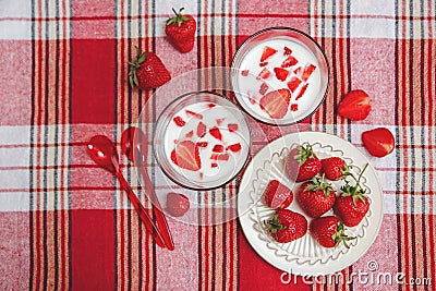 Two Glasses of Yogurt,Red Fresh Strawberries are in the Ceramic Plate with Plastic Spoons on the Check Tablecloth.Breakfast Organi Stock Photo