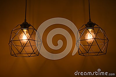 Two glowing modern light bulbs in an iron frame hanging against background of yellow wall inside room Stock Photo