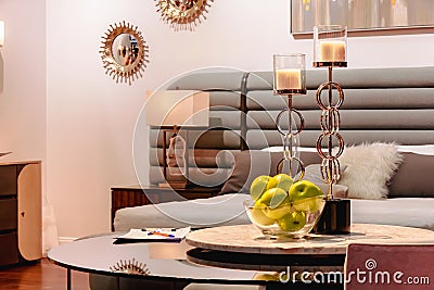 Two golden candlesticks and green apples in a glass vase stand on the table Stock Photo