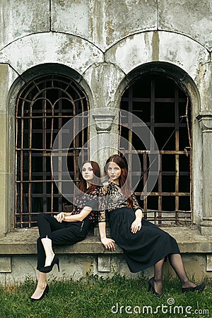 Two gorgeous women in black sitting at old church in the city and posing, stylish gothic themed, ladies party Stock Photo