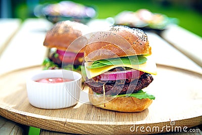 Two gourmet burgers with sauce on the side outdoors. Stock Photo