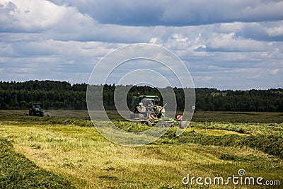 two green haymaking John Deere tractors with Krone plow on summer field before storm - telephoto shot with selective Editorial Stock Photo