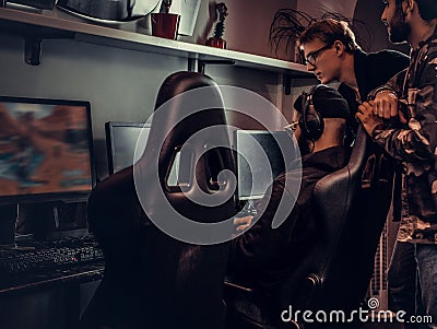 Two guys watch their friend play video games in a gaming club or internet cafe. Stock Photo