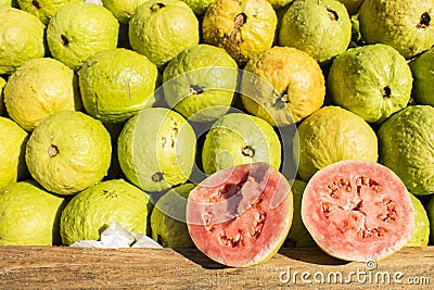 Two halfes of red and bright green wet gavas opened with a stack of fruits behind it Stock Photo