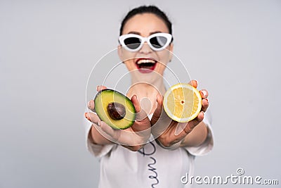 Two halves of avocado and orange in the hands of the girls, sunglasses, smile Stock Photo