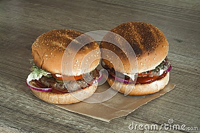 Two hamburgers on sesame buns with succulent beef patties and fresh salad ingredients on crumpled brown paper on a rustic wood ta Stock Photo
