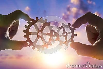 Two hands connect the gears, the details of the puzzle. against the sky with sunset. Stock Photo