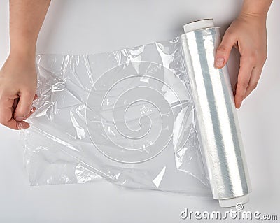 two hands hold a large roll of wound white transparent film for wrapping food Stock Photo