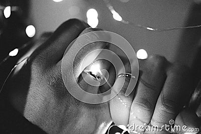 Two hands - a man`s and a woman`s, are tied with a garland of lights. hands with rings, wedding concept, grainy photography Stock Photo