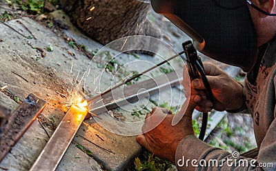 Two hands masked welder welding armature outdoors Stock Photo