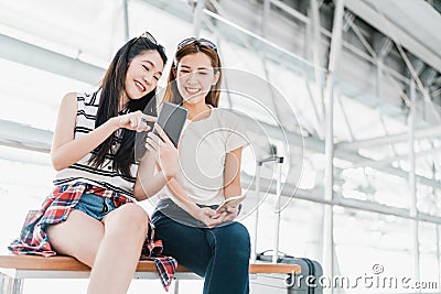 Asian girls using smartphone checking flight or online check-in at airport together, with luggage. Air travel, summer holiday Stock Photo