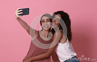 Two happy carefree teenage girl taking selfie looking at smartphone front camera isolated on pink background Stock Photo